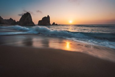 Atlantik kıyısındaki Portekiz Ursa Sahili. Gün batımı yansıması. Beyaz dalga, arka planda kaya silueti olan kumlu sahile doğru yuvarlanıyor. Resimli manzara manzarası