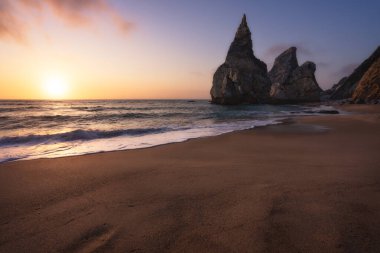Ursa Sahili, Sintra, Portekiz. Akşamları, Atlantik Okyanusu manzarasında yumuşak altın gün batımı ışığı olan kayalıklı kumsal.