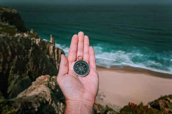 Olhando para a bússola na palma da mão do homem simbolizando o conceito de busca de aventura contra o mar e as ondas na costa no fundo — Fotografia de Stock