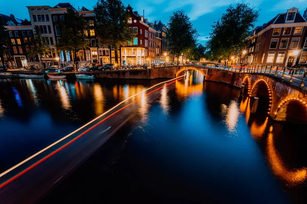 La sera di Amsterdam ha illuminato la città. Sentieri turistici in barca e riflessi del ponte sui canali di Leidsegracht e Keizersgracht. Colpo a lunga esposizione. Viaggio in città concetto visita — Foto Stock