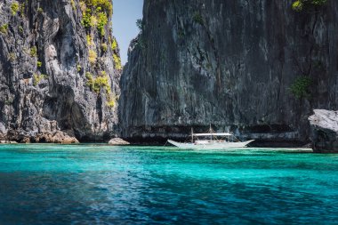 El Nido, Palawan, Filipinler. Okyanus kıyısındaki gizli lagünün girişinde kaya oluşumu ve turizm teknesi.