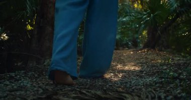 Çıplak ayaklı kadın, güneşli yaz günlerinde sık yeşil ormanda yol boyunca yürür..