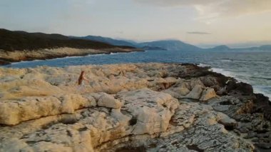 Karanlık Kefalonia 'daki uzak tepelerin üzerine çökerken kadın yalnız başına sarp kıyı şeridinde yürüyor..