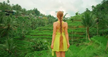 Bali 'nin tropikal kırsalındaki yeşil pirinç teraslarının manzarasıyla yüzleşen kadın..