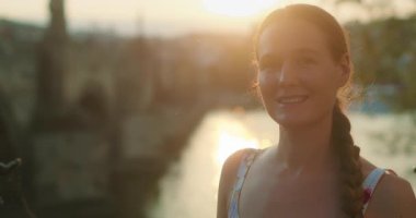 Gülümseyen kadın gün batımında Prag 'da tarihi bir Charles Köprüsü ile Avrupa nehir kıyısında duruyor..