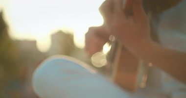 Açık havada altın güneş ışığında gitar çalan erkek ellerinin yakın çekimi..