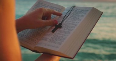 El ele tutuşan İncil deniz kenarında, çapraz kolye yer imi ile..