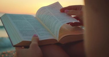 Yazın gün batımında deniz kenarında kitap okurken sayfaları çeviren eller..