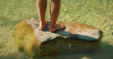 Hırvatistan 'da yaz aylarında Cetina nehrinin berrak sularında kayaların üzerinde duran kişinin ayakları.