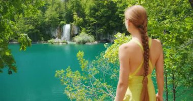 Plitvice Gölleri Ulusal Parkı 'nda huzurlu bir turkuaz göl ve şelaleye hayran bir kadın..