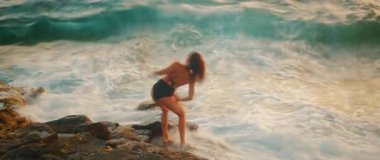 Altın saatinde kayalık sahilde zarif kol hareketleriyle dans eden kadın..