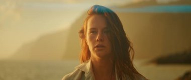 Kadın, sahil kayalıkları tarafından sakin bir ifadeyle kameraya bakıyor..