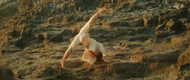 Kadın gün batımında güneşli sahil kayalıklarında akrobatik dans pozu veriyor..