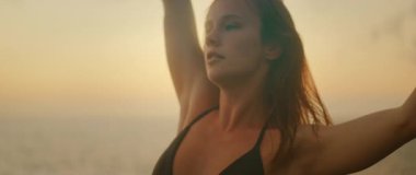 Siyah kıyafetli kadın dansçı, alacakaranlıkta kayalık sahilde akışkan hareketler yapıyor..