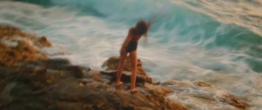 Güçlü dalgaların yanında dans eden kadının bulanık görüntüsü volkanik kayalara çarpıyor..