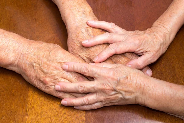 Old people holding hands. Closeup on wooden table.