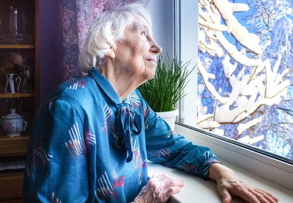 Vieja mujer solitaria sentada cerca de la ventana de su casa. — Foto de Stock