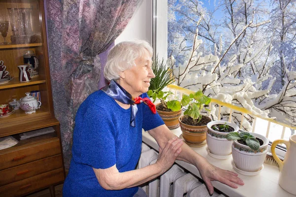 Vieja mujer solitaria sentada cerca de la ventana de su casa. — Foto de Stock