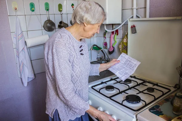 Senior old housewife at home and examines gas and electricity bills — Stock Photo, Image
