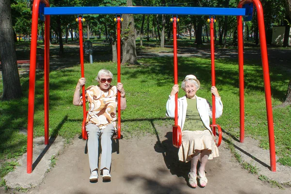 The two mature women in park at swing at summer