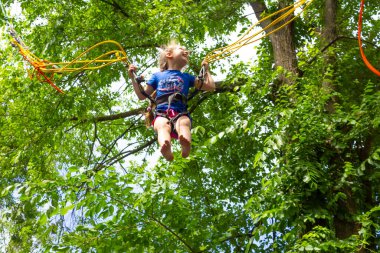 Gülümseyen mutlu kız yeşil ağaçlara karşı trambolinde bungee ile atlıyor.
