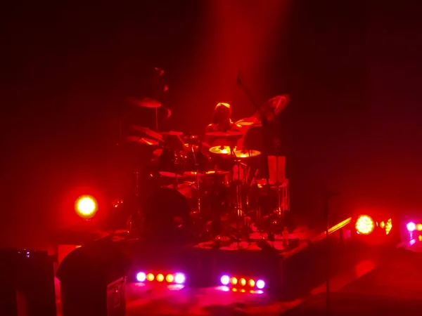 A drummer is on the stage. A man is playing music. Red spotlight. A music event
