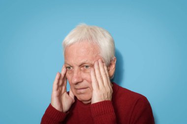 Beyaz saçlı adam mavi arka planda baş ağrısı çekiyor.