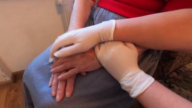 Doktor ellerinin koruyucu eldivenlerle kapanması klinikteki hastane yatağında oturan stresli yaşlı bir kadını rahatlatıyor. Küresel koronavirüs covid-19 sağlık salgını