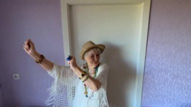 Mutlu gülümseyen komik yaşlı kadın evde boncuk takıp dans ediyor.