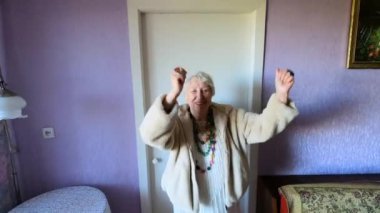 Mutlu gülümseyen komik yaşlı kadın evde boncuk takıp dans ediyor.