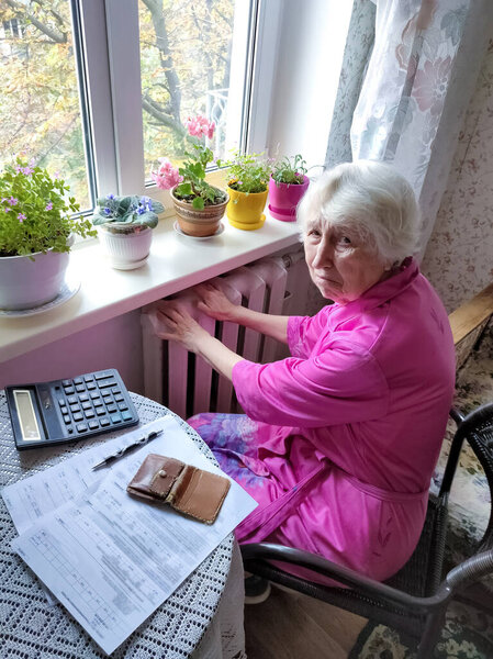 The senior woman holding gas bill in front of heating radiator. Payment for heating in winter.