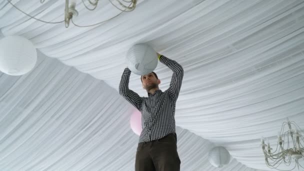 Man Hanging Colorful White Pink Gray Paper Lanterns To Ceiling