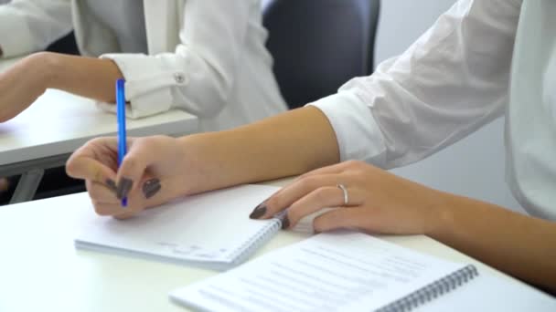 Primer plano joven estudiante escribiendo con bolígrafos en cuaderno en el aula — Vídeos de Stock