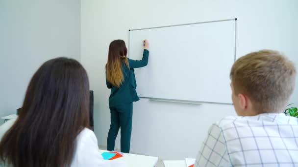 Jovem professor escrevendo para alunos em quadro branco em sala de aula . — Vídeo de Stock