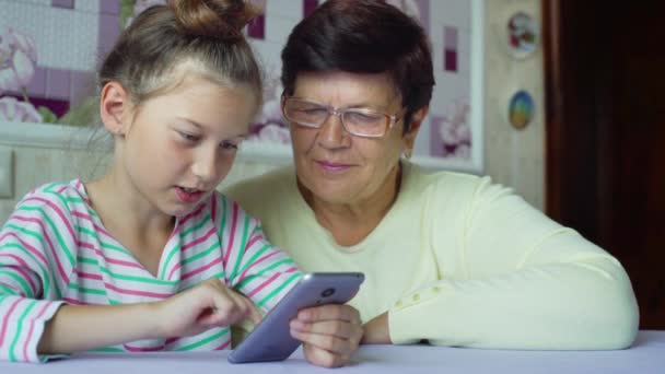 Молодая милая внучка учит бабушку пользоваться смартфоном дома — стоковое видео