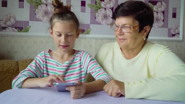 Jeune petite-fille mignonne enseignant à grand-mère comment utiliser un smartphone à la maison — Video