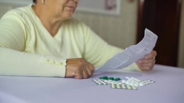 Senior vrouw leest inlichtingenblad voorgeschreven medicijnen zitten aan tafel thuis — Stockvideo