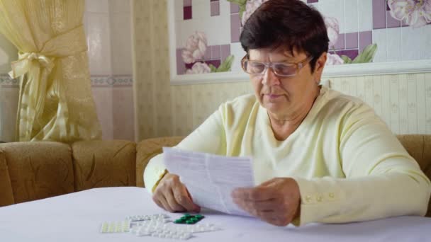 年配の女性が自宅のテーブルに座って処方薬の情報シートを読む — ストック動画