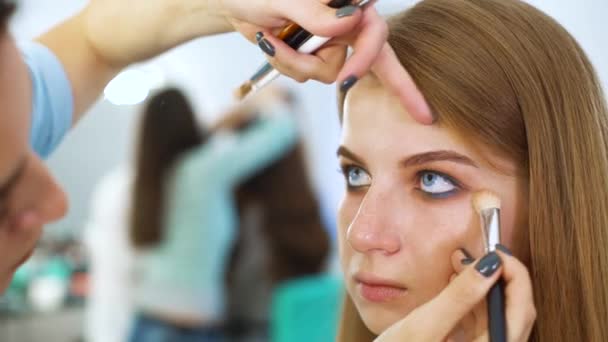 Primer plano artista de maquillaje femenino haciendo maquillaje profesional para la joven mujer de pelo rojo en el salón de belleza — Vídeos de Stock