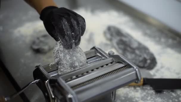 Vista de cerca de las manos del chef en guantes poniendo masa negra en la máquina de pasta y enrollándola manualmente — Vídeos de Stock