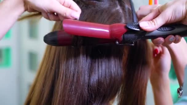 Fechar as mãos femininas usando ferro de ondulação para cabelos longos e escuros — Vídeo de Stock