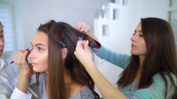 Beauty salon specialista doing professional makeup and hairstyle for young brunette woman — Stock Video