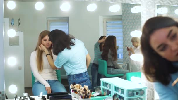 Zrcadlový odraz vizážistka dělá profesionální make-up pro roztomilá mladá žena v beauty salonu — Stock video