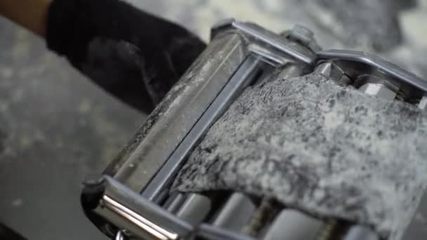 Closeup view of hands in gloves putting black dough in pasta machine and rolling it manually — Stock Video