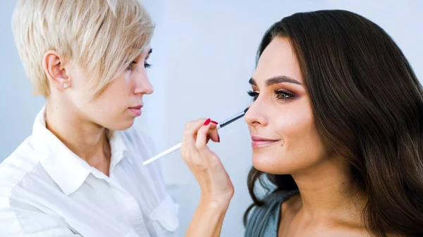 beauty salon specialist doing professional makeup for young brunette woman