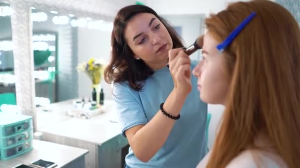 Professionell makeupartist tillämpa makeup till en attraktiv rött hår ung kvinna — Stockvideo