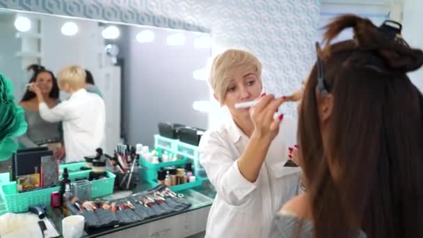 Reflejo espejo de artista de maquillaje femenino haciendo maquillaje profesional de mujer linda en salón de belleza — Vídeos de Stock