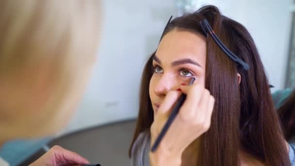 Primer plano de artista de maquillaje aplicando sombras de ojos con cepillo en la cara de las mujeres jóvenes en el salón de belleza — Vídeos de Stock