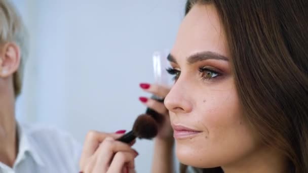 Close-up vista da menina modelo recebendo maquiagem profissional pelo artista de maquiagem no salão de beleza — Vídeo de Stock