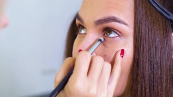 Primer plano de la cara de la mujer joven conseguir maquillaje de ojos profesional por artista de maquillaje femenino — Vídeos de Stock